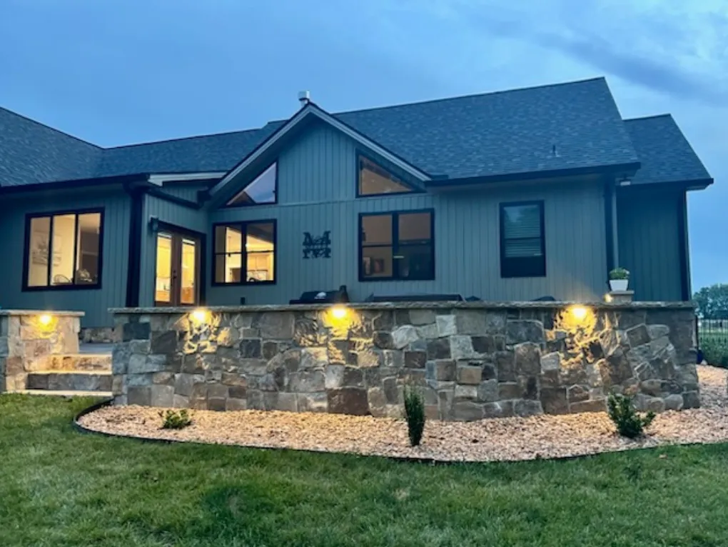 Modern home exterior with blue siding and natural stone veneer base with landscape lighting
