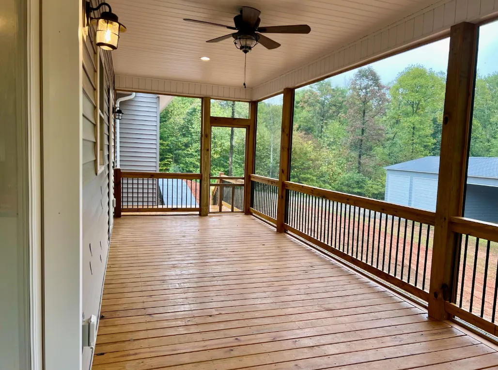 Screened porch with ceiling fan and outdoor dining area overlooking trees