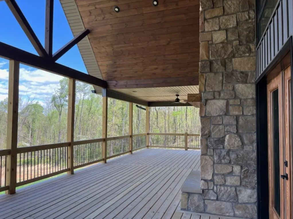 Large covered porch with stone columns, wood ceiling, and ceiling fans